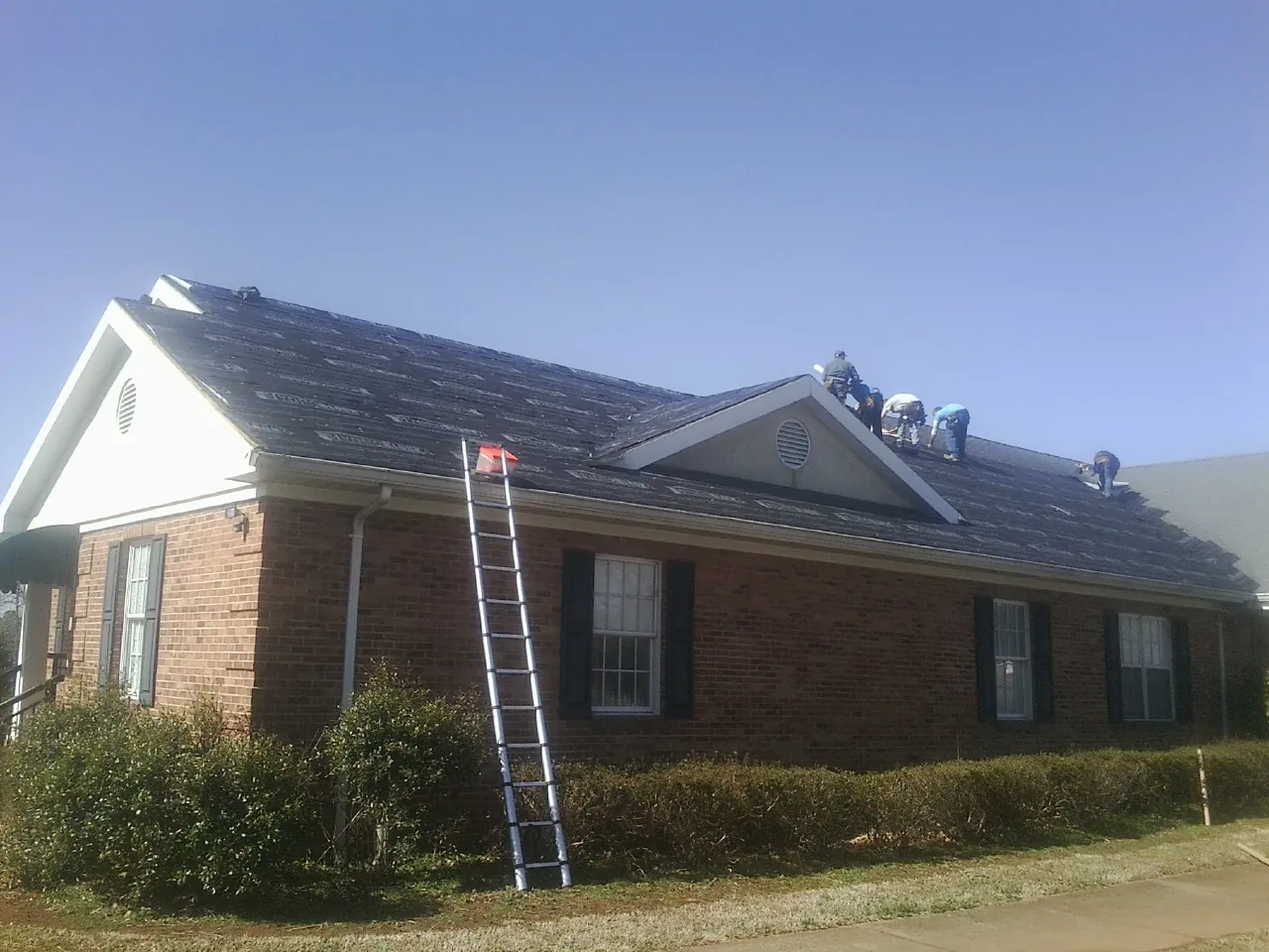 Crew tearing shingles off a brick ranch roof with a ladder set — Metal Roof Repair work by our crew in Ingleside
