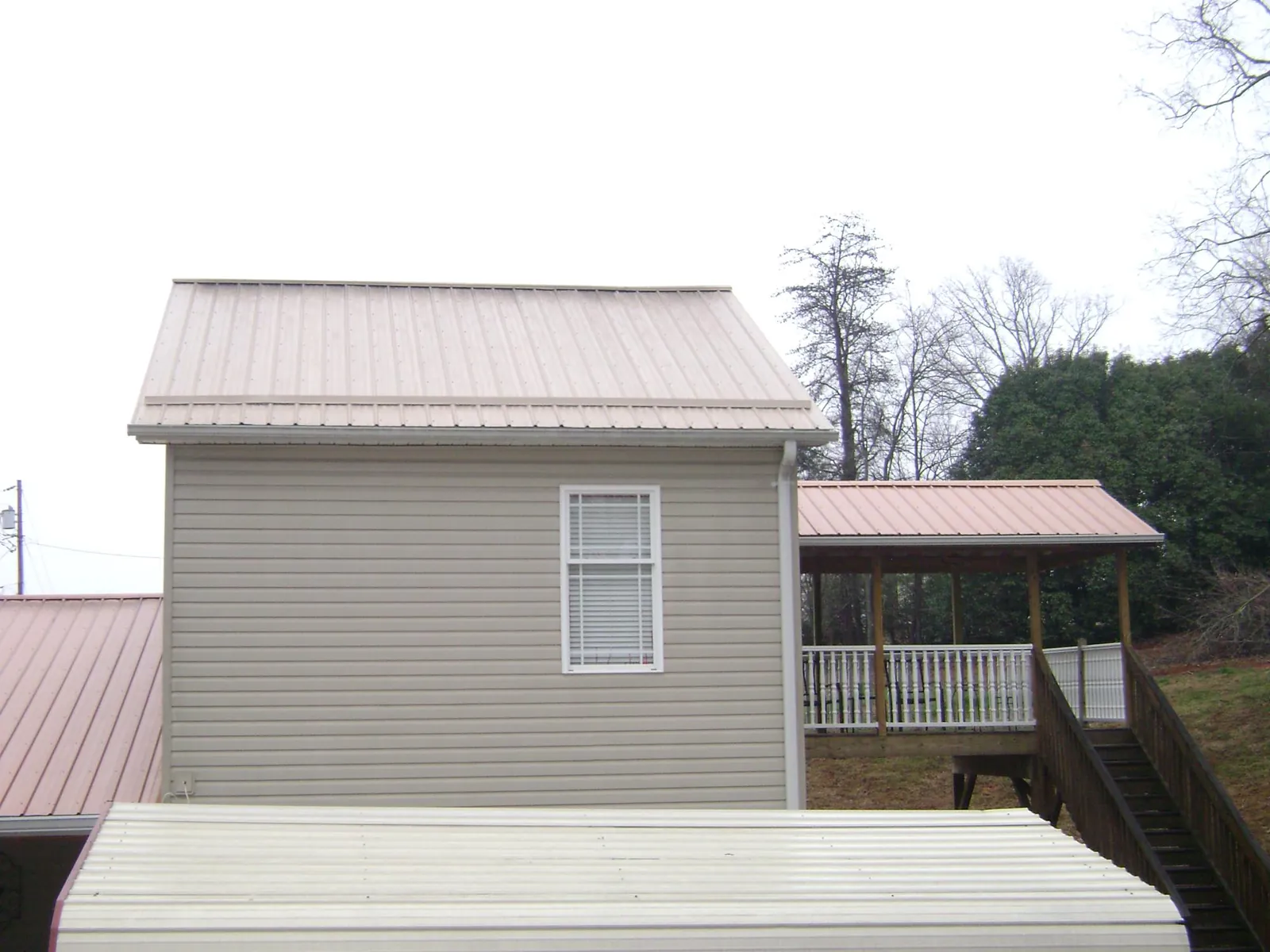 Tan metal roofs on a two story addition and attached porch, from a Roof Replacement job in Ingleside